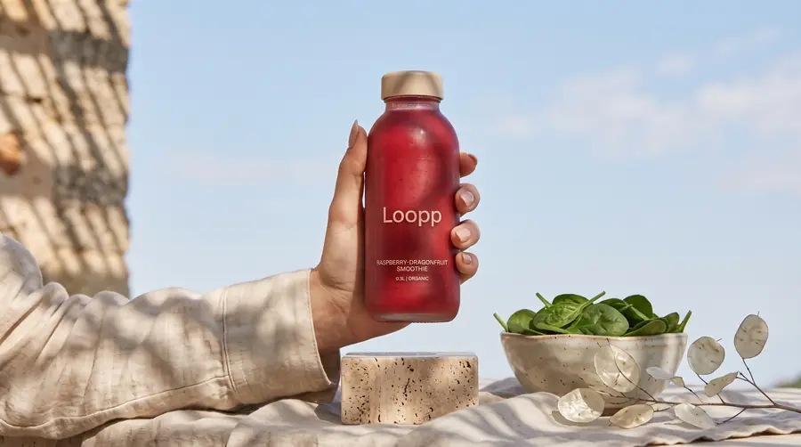 Hand hält eine Flasche Loopp Raspberry-Dragonfruit vor einer Steinmauer